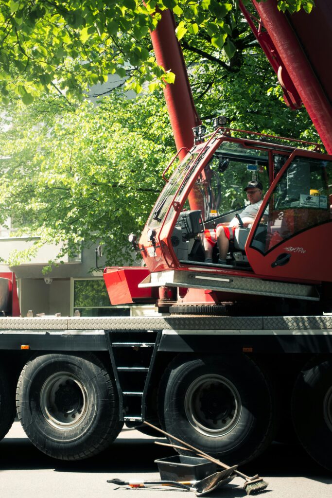 Crane operator in cab, surrounded by nature and machinery in sunny weather.